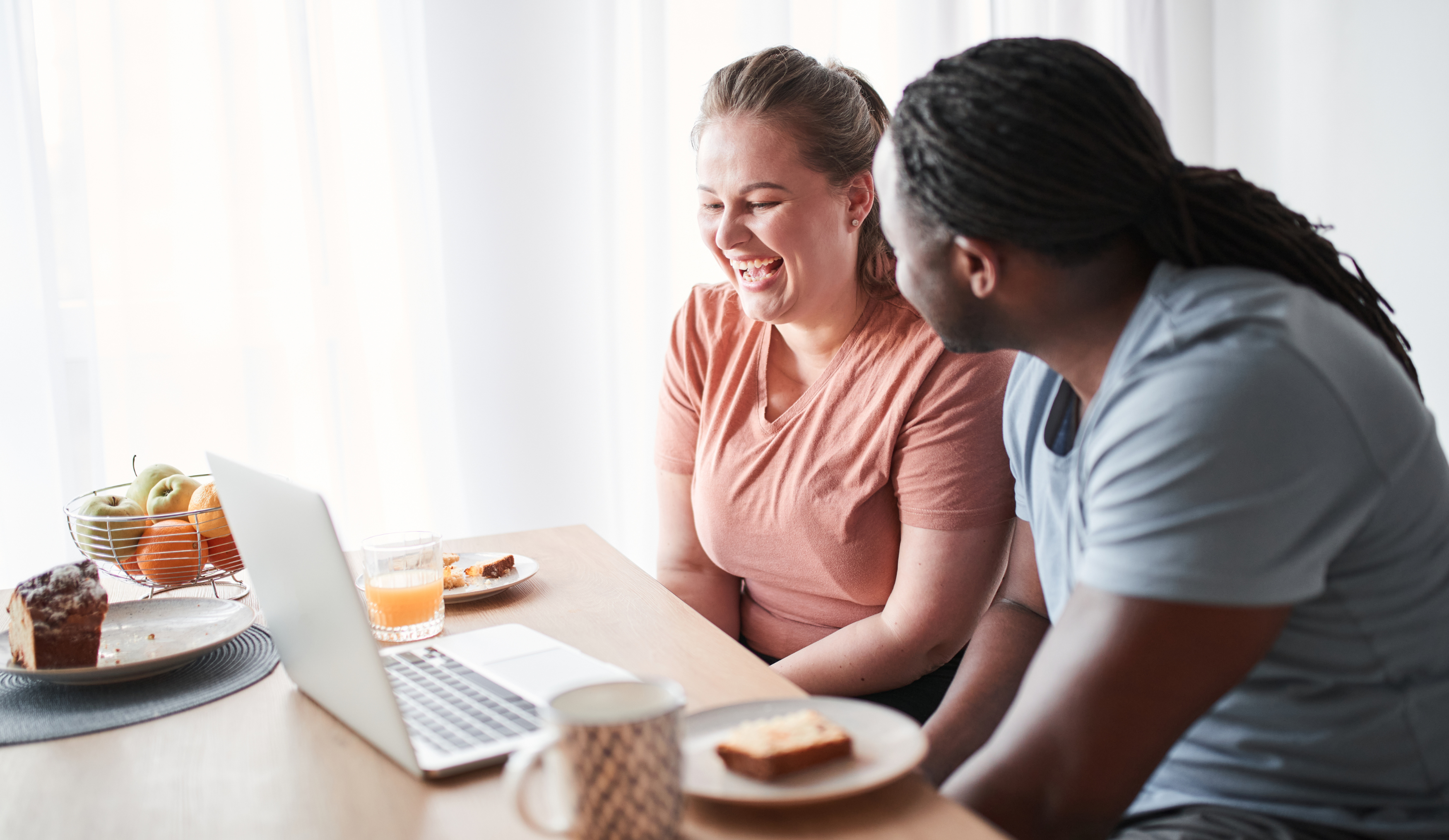 Relieved couple smiling and looking at a computer while eating breakfast.